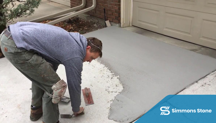 Worker applying spray texture concrete overlay in front of a garage